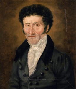Das von einem unbekannten Maler in Ölfarben gemalte Portrait von E.T.A. Hoffmann. Darauf ist ein weißer Mann mit schwarzem, krausen Haar zu sehen. Er trägt einen schwarzen Mantel mit mehreren Metallknöpfen und ein weißes Rüschenhemd.